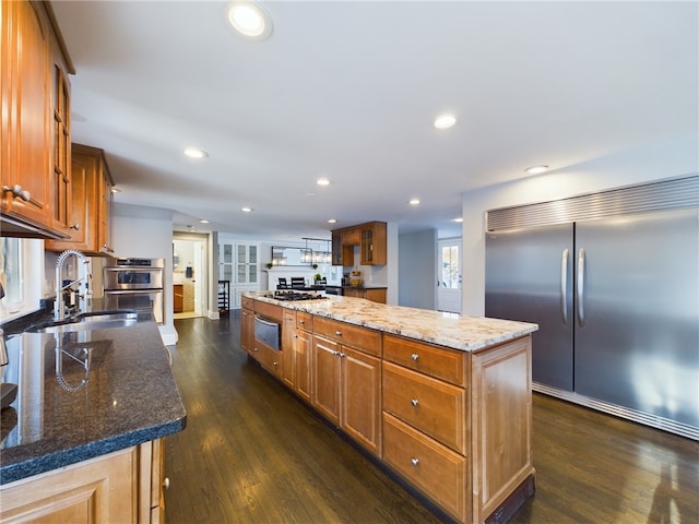 kitchen featuring stainless steel appliances, a sink, a center island, brown cabinetry, and dark wood finished floors