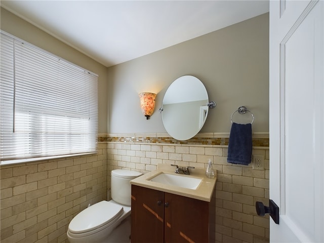 bathroom with toilet, a wainscoted wall, tile walls, and vanity