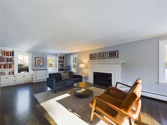 living area featuring dark wood-type flooring, baseboard heating, built in shelves, and a fireplace with flush hearth