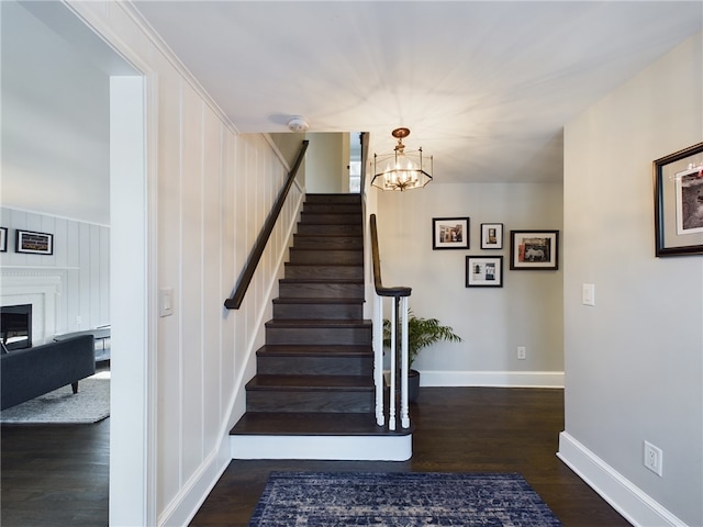 stairway featuring a notable chandelier, a fireplace, wood finished floors, and baseboards