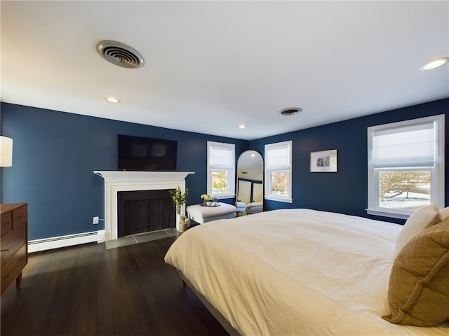 bedroom featuring a fireplace with flush hearth, visible vents, baseboard heating, and wood finished floors