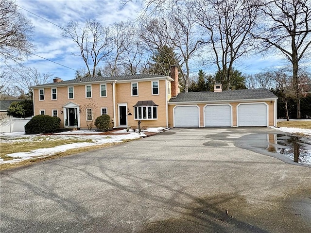 colonial-style house featuring driveway, a chimney, and an attached garage