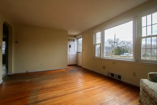 empty room featuring light wood-type flooring, arched walkways, visible vents, and baseboards