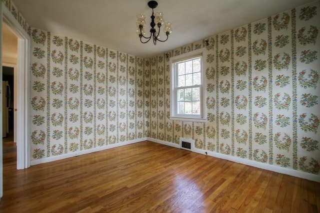 unfurnished room featuring a notable chandelier, wood finished floors, visible vents, baseboards, and wallpapered walls