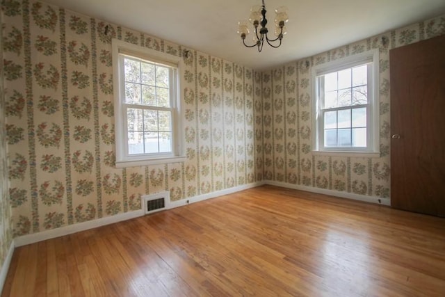 empty room featuring light wood-style floors, visible vents, baseboards, and wallpapered walls