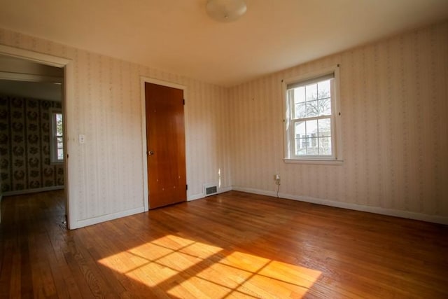 empty room with baseboards, wood-type flooring, visible vents, and wallpapered walls