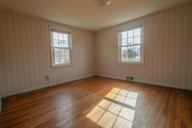 empty room featuring wallpapered walls, baseboards, visible vents, and hardwood / wood-style floors