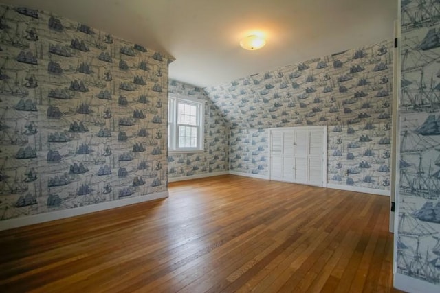 additional living space featuring wallpapered walls, baseboards, vaulted ceiling, and hardwood / wood-style floors