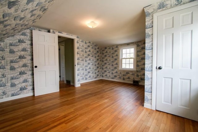 spare room with baseboards, vaulted ceiling, light wood finished floors, and wallpapered walls