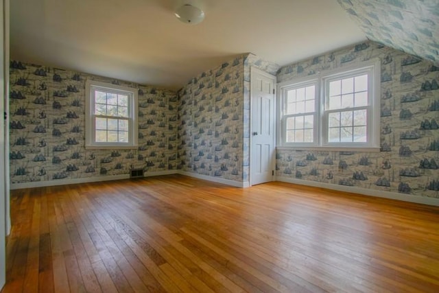 empty room featuring wallpapered walls, baseboards, visible vents, and hardwood / wood-style floors