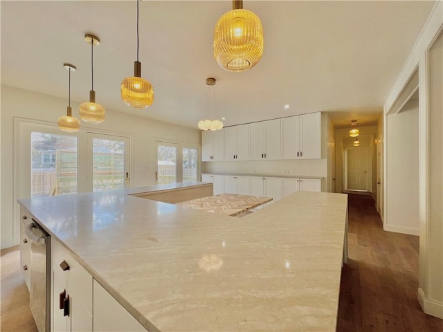 kitchen featuring light stone counters, a spacious island, hanging light fixtures, white cabinets, and wood finished floors