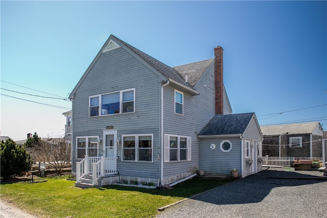 rear view of property with a shingled roof, a chimney, and a lawn