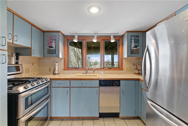 kitchen featuring a sink, light countertops, appliances with stainless steel finishes, backsplash, and glass insert cabinets