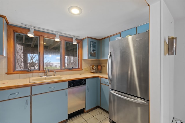 kitchen with stainless steel appliances, tasteful backsplash, light countertops, a sink, and blue cabinets