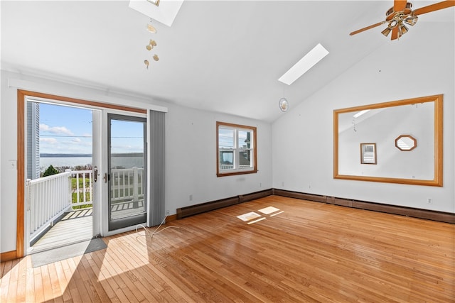 interior space featuring light wood-style flooring, a ceiling fan, a baseboard heating unit, vaulted ceiling with skylight, and baseboards