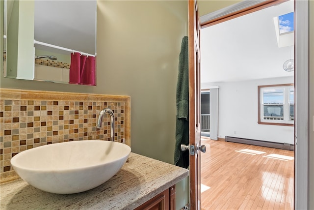 full bathroom featuring a baseboard radiator, a skylight, wood finished floors, vanity, and backsplash