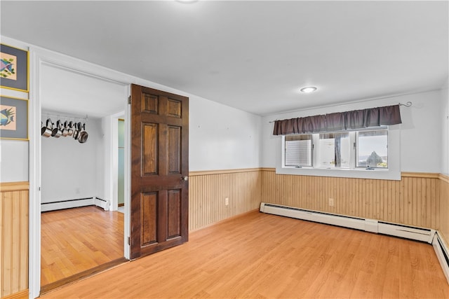 spare room with wainscoting, baseboard heating, and wood finished floors