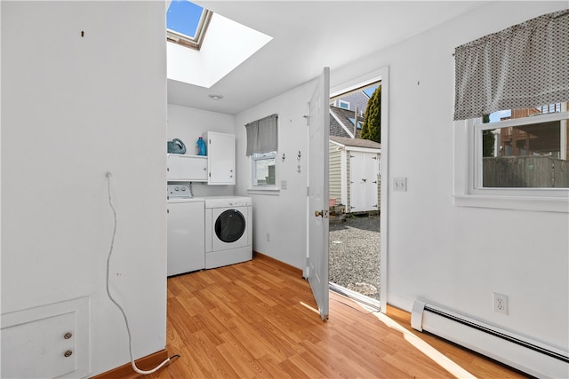 washroom featuring a skylight, washing machine and clothes dryer, a baseboard radiator, cabinet space, and light wood-type flooring