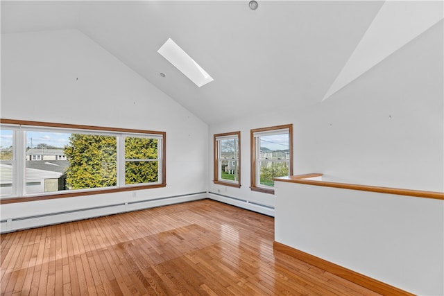 empty room featuring a skylight, high vaulted ceiling, baseboard heating, and light wood-style floors