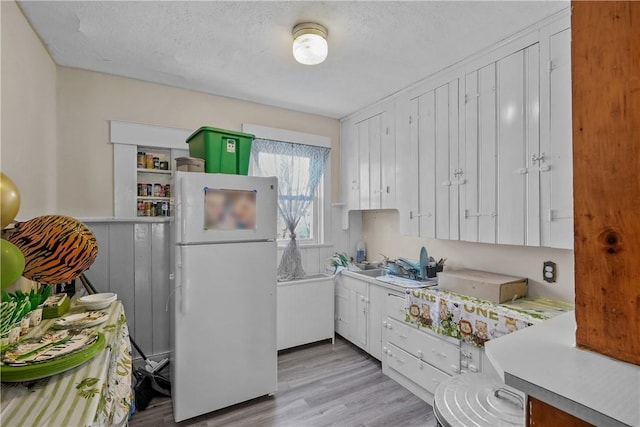 kitchen featuring light wood finished floors, light countertops, freestanding refrigerator, white cabinets, and a textured ceiling