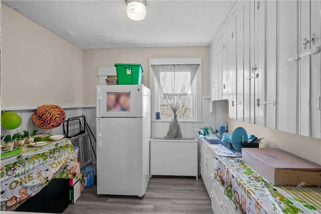 kitchen featuring freestanding refrigerator, white cabinetry, and wood finished floors