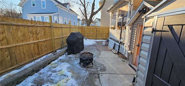 snow covered patio with an outdoor fire pit, a grill, and a fenced backyard