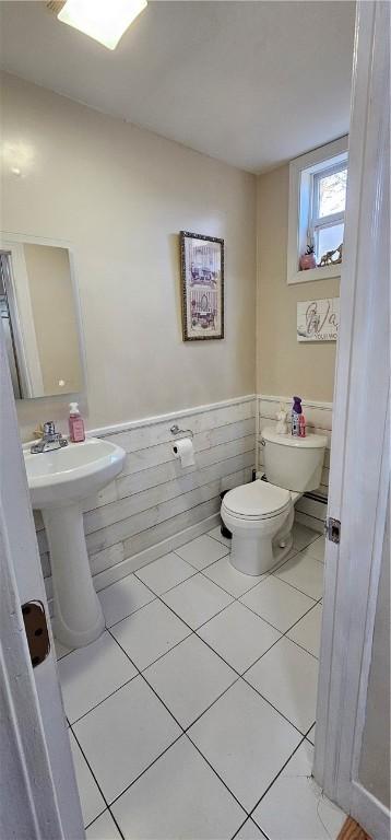 half bathroom featuring a wainscoted wall, tile patterned flooring, and toilet