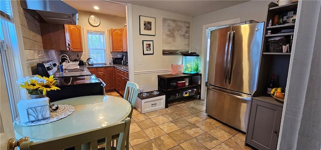 kitchen with brown cabinets, backsplash, freestanding refrigerator, ventilation hood, and a sink