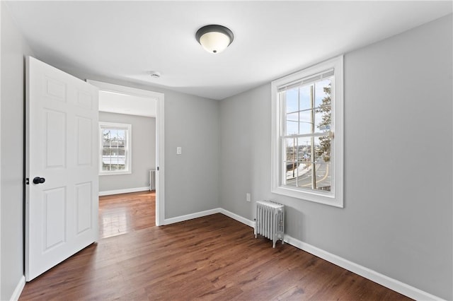 empty room featuring dark wood-style floors, baseboards, and radiator