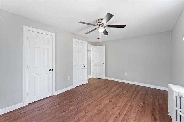 unfurnished bedroom with dark wood-style flooring, baseboards, and radiator heating unit