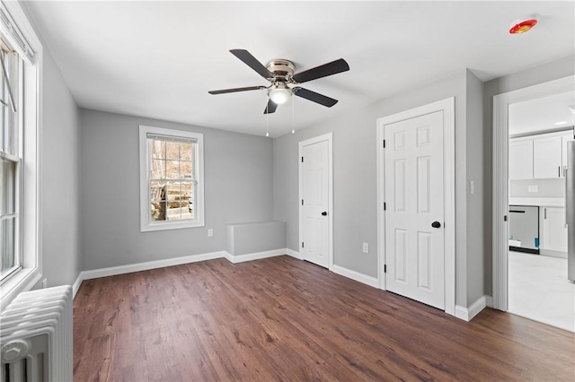 unfurnished bedroom featuring radiator heating unit, dark wood finished floors, two closets, and baseboards