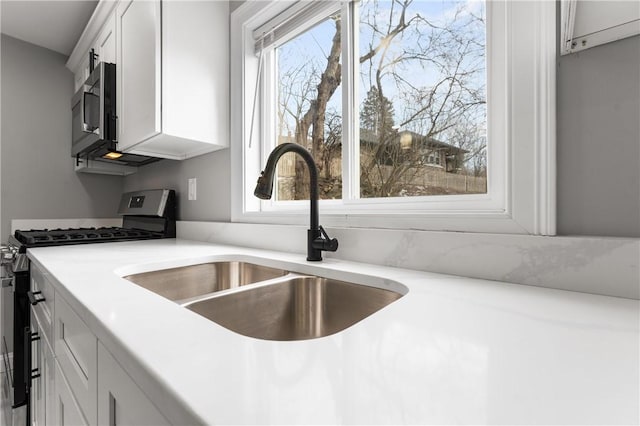 kitchen featuring stainless steel appliances, light countertops, a sink, and white cabinetry