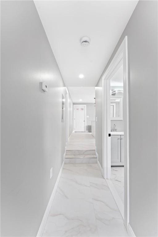 corridor with marble finish floor, baseboards, and a sink