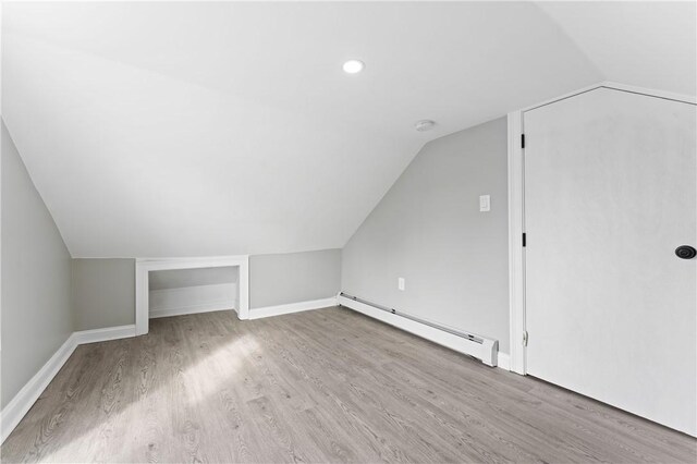 bonus room featuring light wood-type flooring, a baseboard radiator, vaulted ceiling, and baseboards