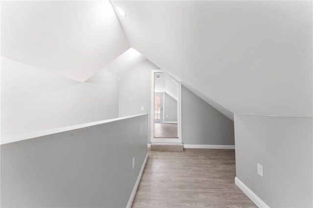 additional living space featuring light wood-type flooring, lofted ceiling, and baseboards