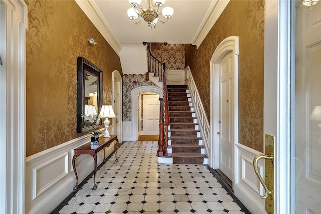 foyer entrance featuring wallpapered walls, arched walkways, crown molding, and wainscoting