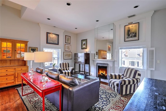 living area featuring a warm lit fireplace, dark wood-type flooring, and visible vents