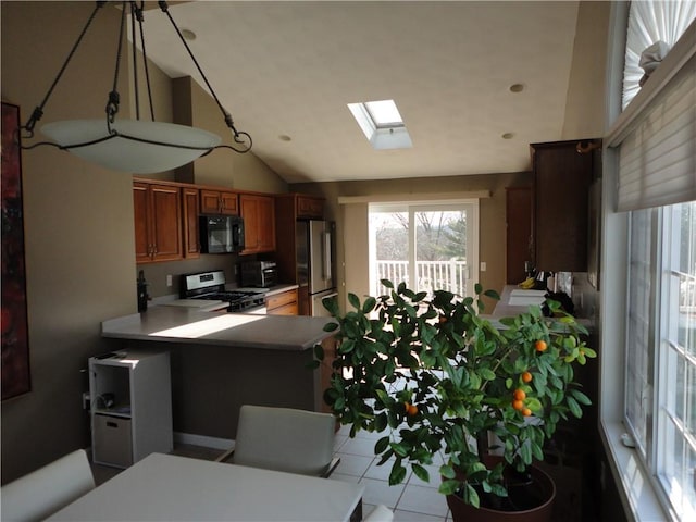 kitchen with a peninsula, a skylight, light countertops, appliances with stainless steel finishes, and brown cabinets