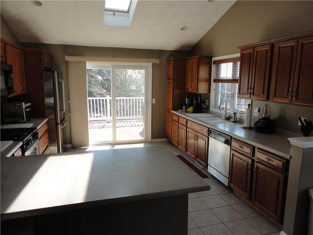 kitchen with stainless steel appliances, light countertops, lofted ceiling with skylight, light tile patterned flooring, and a sink