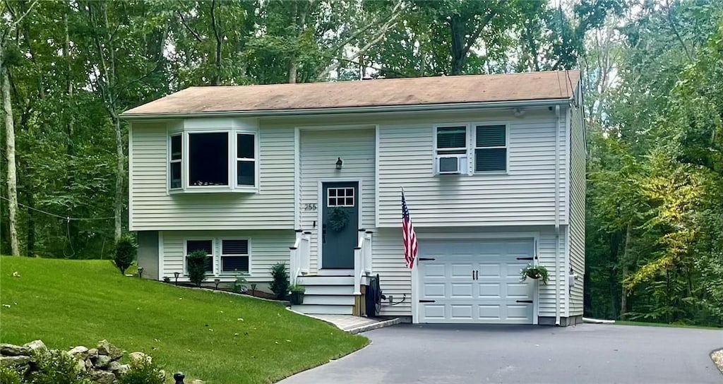 raised ranch with an attached garage, aphalt driveway, and a front lawn