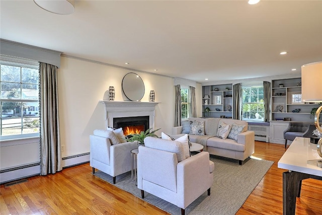 living area featuring a warm lit fireplace, light wood-style flooring, ornamental molding, a baseboard heating unit, and recessed lighting