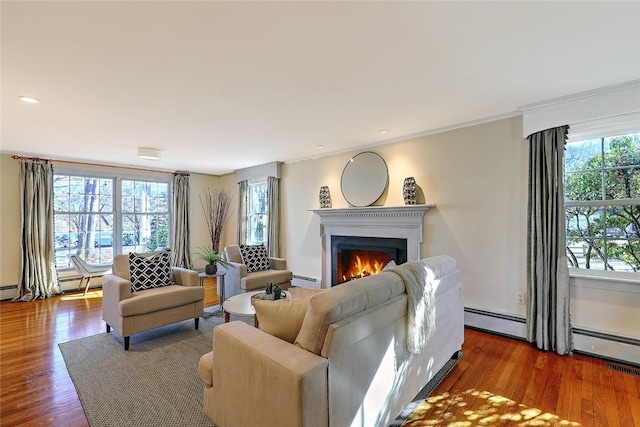 living area with a warm lit fireplace, a baseboard heating unit, ornamental molding, and wood finished floors