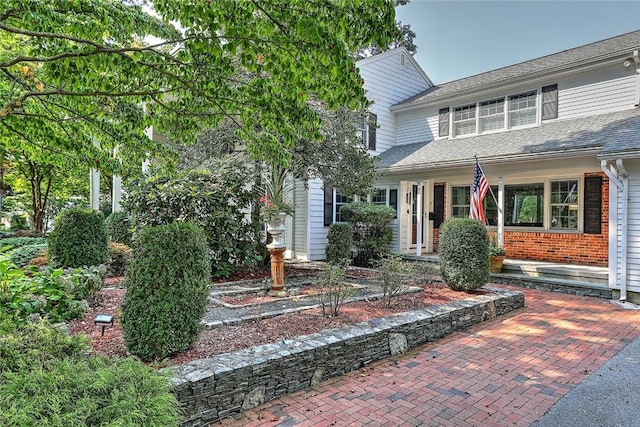 view of front of property with a shingled roof and brick siding