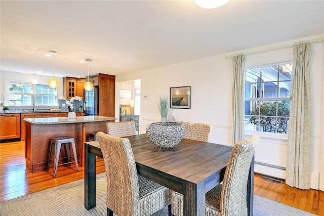 dining area with light wood finished floors, visible vents, and baseboard heating