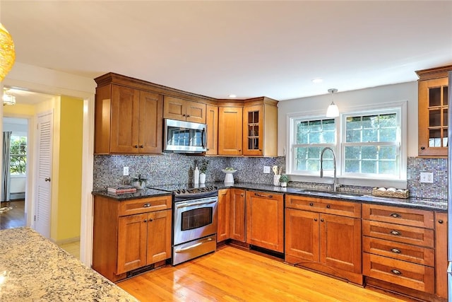 kitchen with dark stone counters, appliances with stainless steel finishes, a sink, and brown cabinets