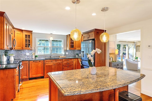 kitchen featuring a sink, light wood-style floors, appliances with stainless steel finishes, brown cabinets, and glass insert cabinets