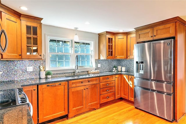 kitchen featuring light wood-style flooring, a sink, brown cabinets, dark stone countertops, and stainless steel fridge