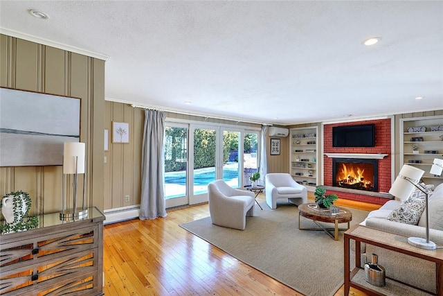 living room with built in shelves, a baseboard heating unit, a fireplace, a wall mounted AC, and light wood finished floors