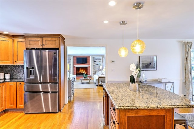 kitchen featuring light stone counters, a center island, brown cabinetry, light wood-style floors, and stainless steel fridge with ice dispenser