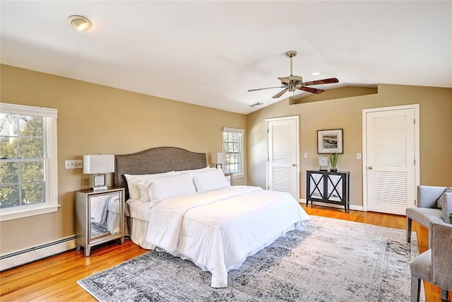 bedroom with visible vents, lofted ceiling, light wood-type flooring, a baseboard heating unit, and two closets